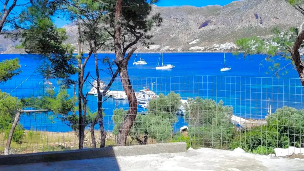 Sea view terrace overlooking Telendos Bay with sailboats and crystal-clear Aegean waters